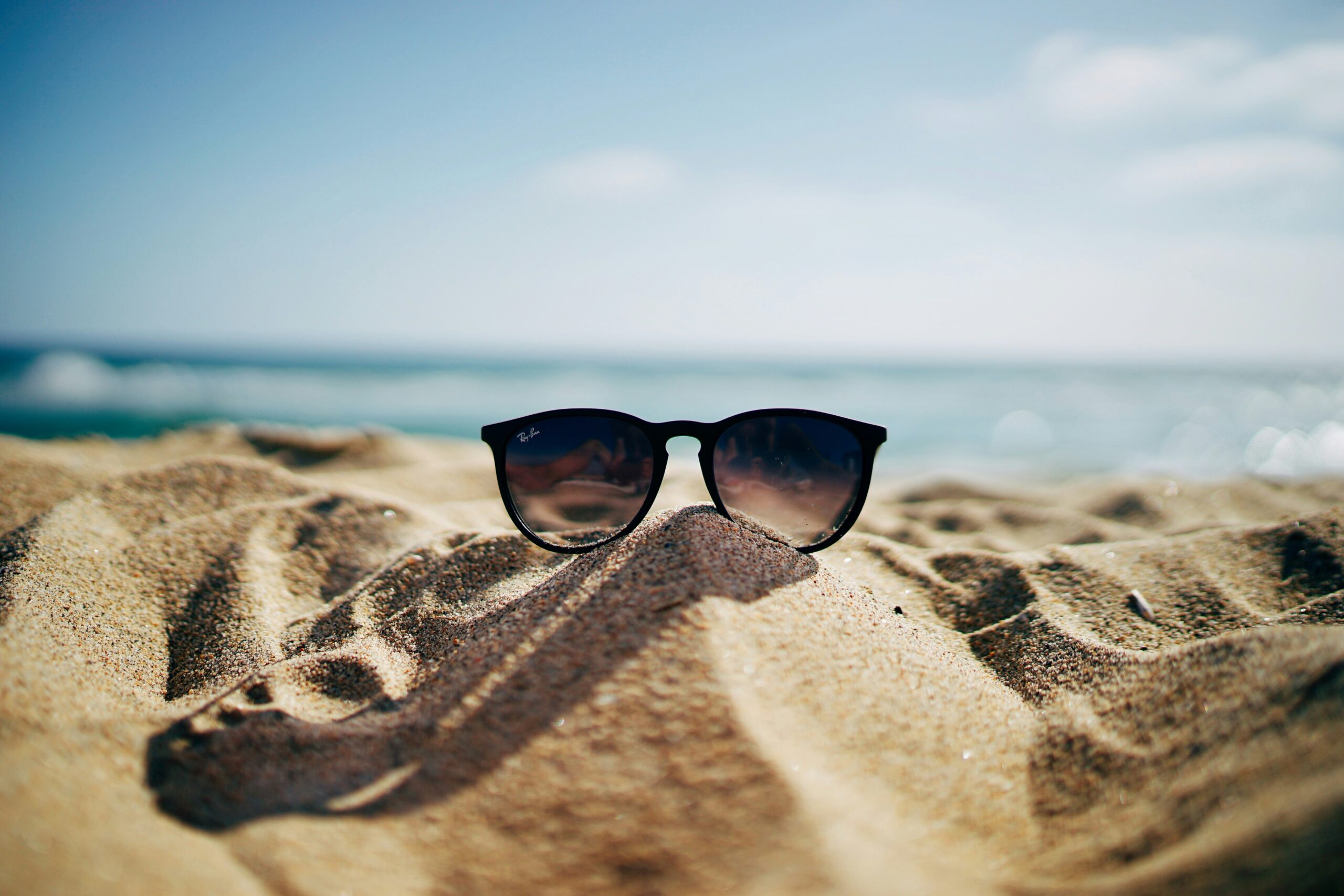 sunglasses sit on a sandy beach