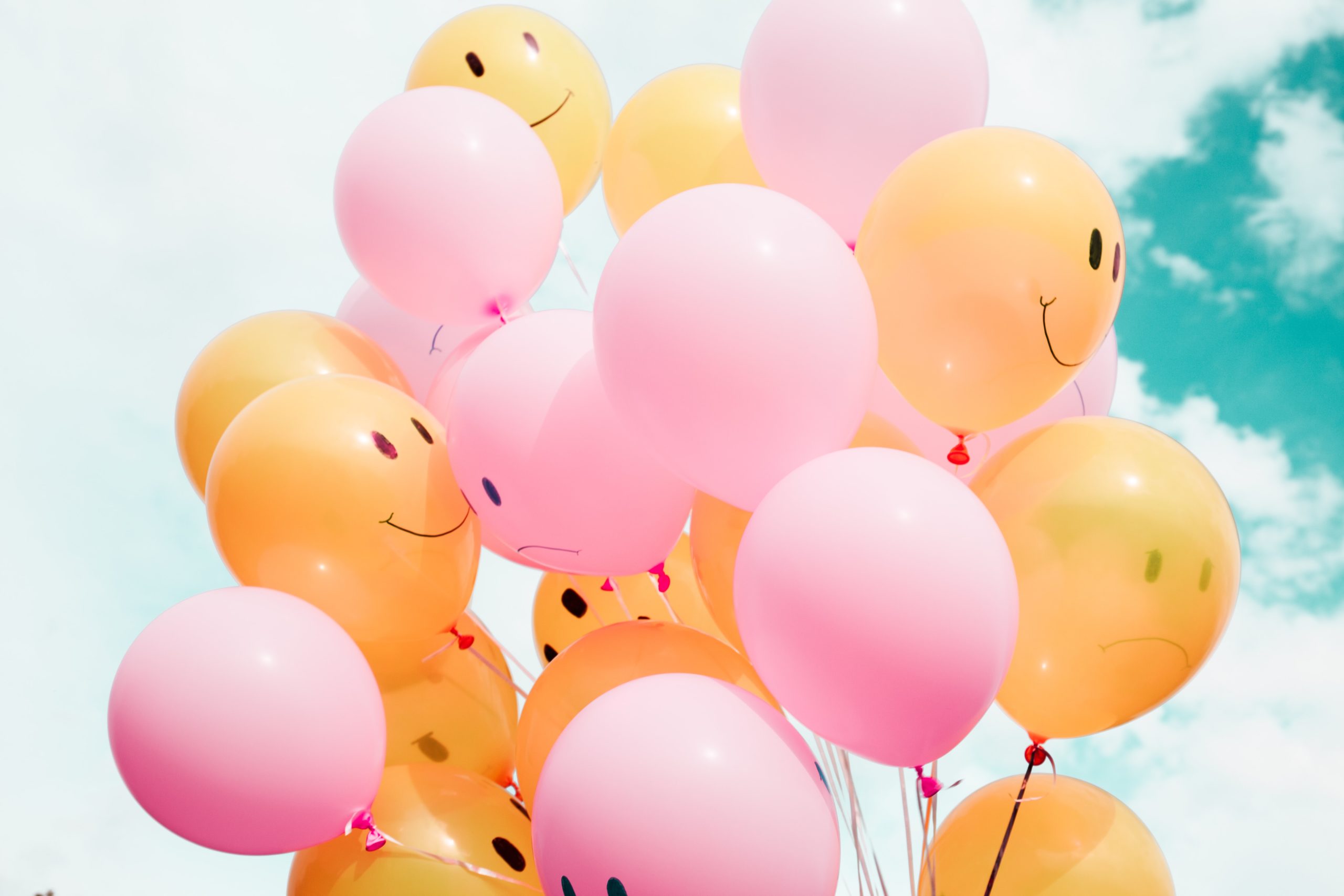 orange and pink smiley face balloons float in a blue sky